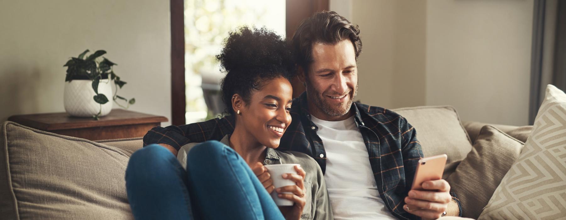 a man and woman sitting on a couch and looking at a cell phone